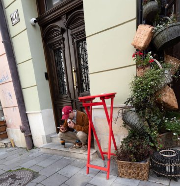 Lviv, Ukrayna - Haziran. 01, 2025: Bir adam dekoratif bir cephede içki ve telefonla bir anın tadını çıkarıyor.