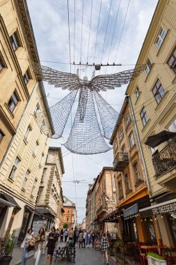 Lviv, Ukrayna - Haziran. 01, 2025: Lviv 'deki pitoresk bir sokak sahnesinde binalar ve başınızın üzerinde asılı duran dekoratif bir melek heykeli yer alıyor.