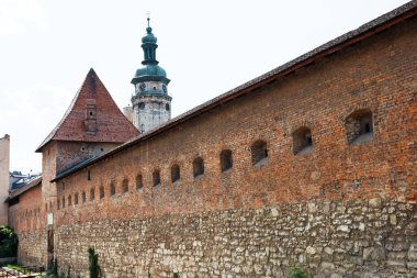 Lviv, Ukrayna - Haziran. 01, 2025: Arka planda belirgin saat kulesi olan tarihi bir binanın tarihi savunma duvarı.