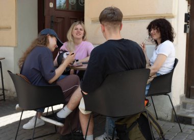 Lviv, Ukrayna - Haziran. 01, 2025: Bir grup arkadaş bir kafede oturmuş, birbirlerinin arkadaşlığından ve güneşli günlerinden zevk alıyorlar.