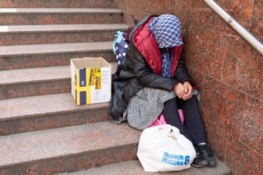 Lviv, Ukrayna - Haziran. 01, 2025: Evsiz biri merdivenlerde elinde bir çanta ve karton kutuyla duruyor, şehirdeki sosyal sorunları vurguluyor.