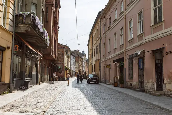 Lviv, Ukrayna - Haziran. 01, 2025: Lviv 'de tarihi binaların ve güneşli bir günün tadını çıkaran birkaç kişinin bulunduğu pitoresk bir kaldırım taşı caddesi.