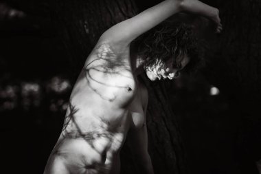 Genç bir kadın gölgelerle çevrili çıplak, siyah beyaz bir fotoğraf çekiyor..