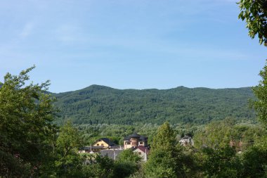Bereketli yeşil dağlar, berrak mavi bir gökyüzü ve yeşilliklerin ortasındaki evleri gösteren manzaralı bir manzara..