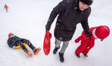 KYIV, UKRAINE - 30 Ocak 2021: Aileler ve çocuklar şehir parkındaki karlı bir tepeden neşeyle kayıyorlar. Eğlenceli ve canlı bir kış günü için parlak plastik kızaklar kullanıyorlar..