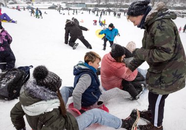 KYIV, UKRAINE - 30 Ocak 2021: Aileler ve çocuklar şehir parkındaki karlı bir tepeden neşeyle kayıyorlar. Eğlenceli ve canlı bir kış günü için parlak plastik kızaklar kullanıyorlar..