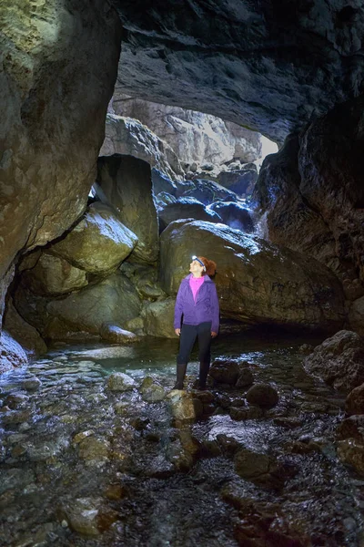 背着背包徒步旅行到一个有河流的山洞里的女人 — 图库照片