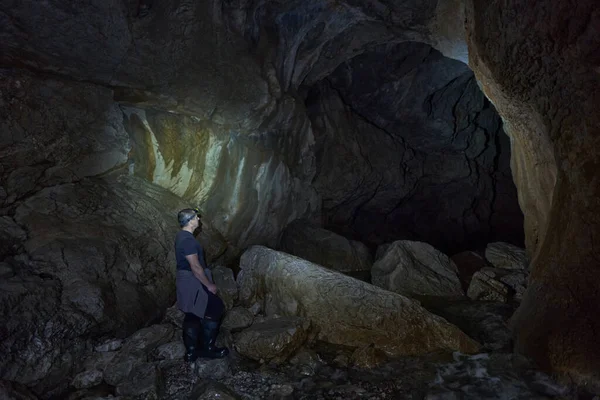 Man with headlamp hiking into a cave with a river