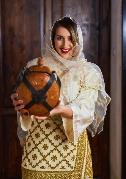 年轻的罗马尼亚女人穿着传统的新娘流行服装 住在一个古老的家里 手里拿着一个木瓶 — 图库照片