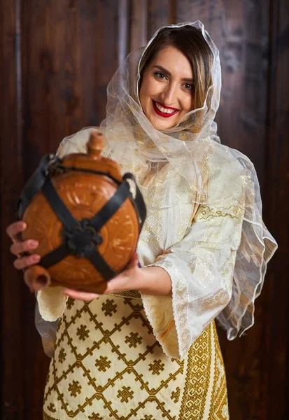 年轻的罗马尼亚女人穿着传统的新娘流行服装 住在一个古老的家里 手里拿着一个木瓶 — 图库照片