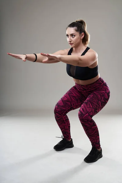 Plus size young woman doing isometric fitness exercises on gray background