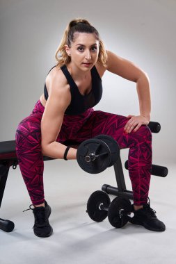 Kendine güveni tam, kilolu bir kadın spor salonundaki halterlerle çalışıyor. Gri arka planda izole edilmiş.