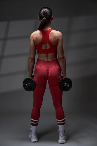 運動能力の若いモデルの女性の赤いジムの服がうまくいきます 背景に影の投影とスタジオ照明 — ストック写真