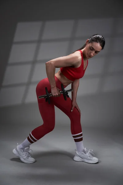 運動能力の若いモデルの女性の赤いジムの服がうまくいきます 背景に影の投影とスタジオ照明 — ストック写真