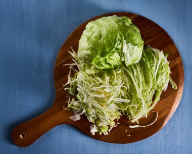 Chopped and halved fresh white cabbage on a wooden cutting board on blue background