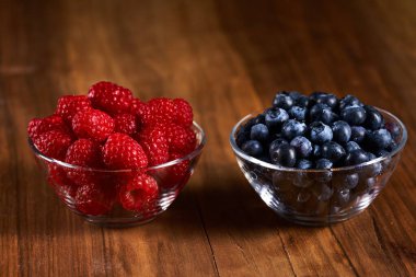 Raspberries and blueberries in bowls on a wooden board