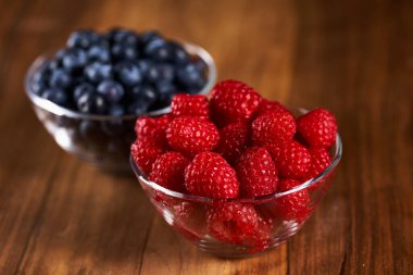 Raspberries and blueberries in bowls on a wooden board
