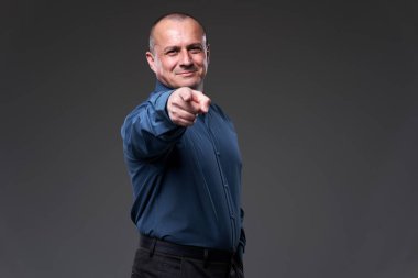 Smiling businessman pointing at the camera, as if choosing the viewer amongst everyone else on gray background