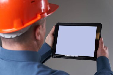 Engineer in hardhat doing planning digitally with a tablet, gray background