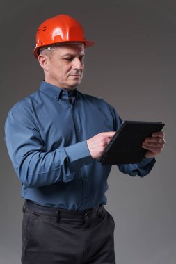 Engineer in hardhat doing planning digitally with a tablet, gray background