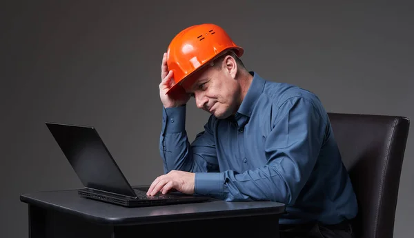 Disappointed and frustrated engineer in hardhat and business suit checking inefficient progress on his laptop