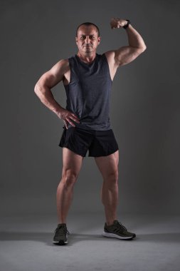 Olgun bir adamın gri arka planda spor yaparken tüm vücudunu çekmesi.