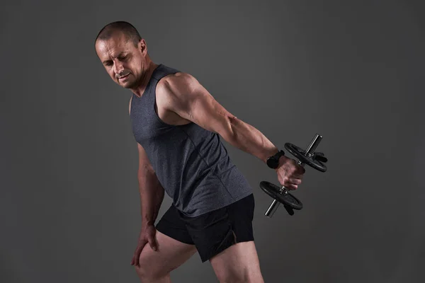 成熟したCaucasian筋肉男でティーとショートパンツ行いますフィットネストレーニング上の灰色の背景 — ストック写真