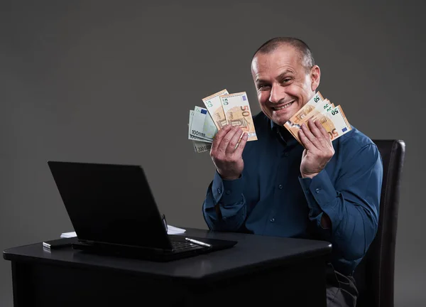 幸せな成熟したビジネスマン現金を保持し 彼の机に座って 富の概念的なイメージ 良い収入 — ストック写真