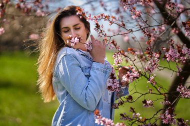 Doğu Asyalı genç bir kadın çiçek açan ağaçlarla parkın tadını çıkarıyor.
