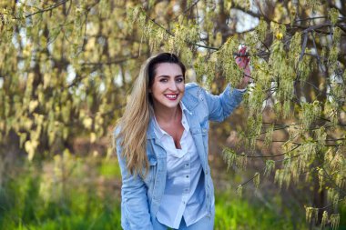 Doğu Asyalı genç bir kadın çiçek açan ağaçlarla parkın tadını çıkarıyor.