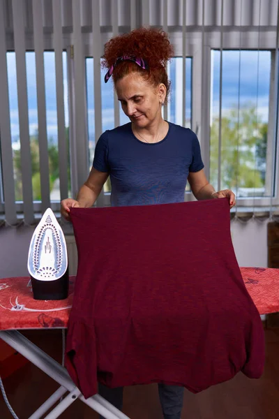 Kręcone Włosy Ruda Gospodyni Domowa Prasowanie Ubrania Przez Okno — Zdjęcie stockowe