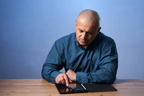 Olgun Bir Adamı Masasında Tabletiyle Mavi Arka Planda Oturuyor — Stok fotoğraf