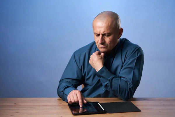 Ώριμος Επιχειρηματίας Κάθεται Στο Γραφείο Του Tablet Του Μπλε Φόντο — Φωτογραφία Αρχείου
