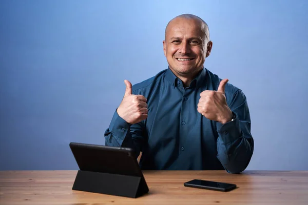 快乐的生意人带着他的平板电脑站在桌子前 背景是蓝色的 — 图库照片