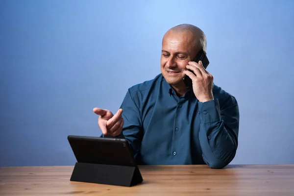 Šťastný Obchodník Telefonem Konverzace Při Pohledu Jeho Tablet Modrém Pozadí — Stock fotografie
