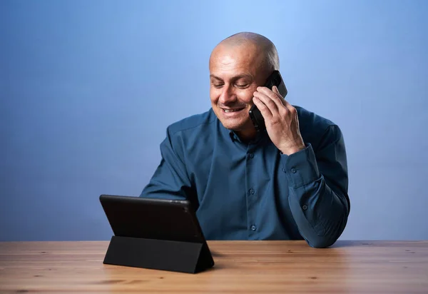 Szczęśliwy Biznesmen Rozmawiający Przez Telefon Patrząc Swój Tablet Niebieskim Tle — Zdjęcie stockowe