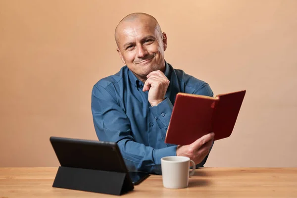 成熟したビジネスマン彼のコーヒーブレイクで本を読んで彼の机で仕事で 流行の背景の上 — ストック写真