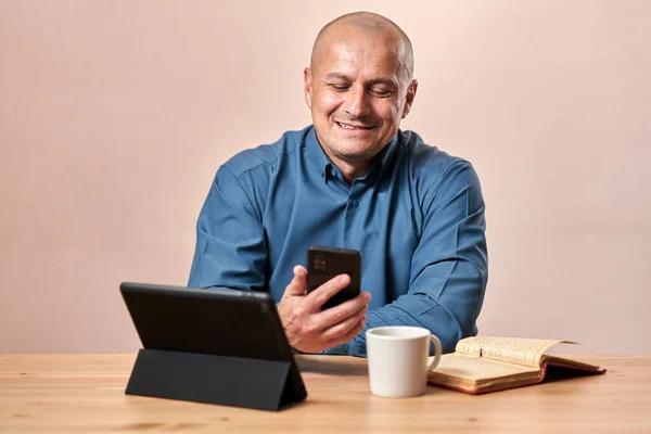 電話とタブレットとコーヒーを飲みながら机の上に座っている幸せな成熟したビジネスマン — ストック写真