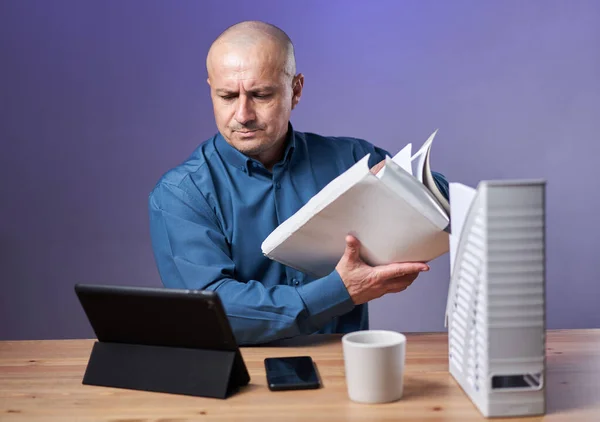 紫色の背景の上に 彼の机の上にファイルやフォルダやタブレットで作業ビジネスマン — ストック写真