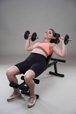 Kendine güveni tam ve kilolu genç bir kadın halterle spor yapıyor.