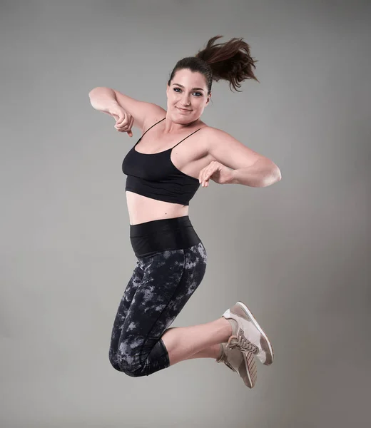 年轻自信加身材的女人穿着体操服跳得很高 灰色背景 — 图库照片