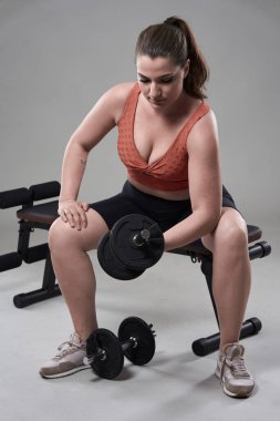 Kendine güveni tam ve kilolu genç bir kadın halterle spor yapıyor.