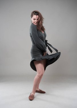 Gri arka planda kendine güvenen, iri yarı genç bir kadının stüdyo portresi.