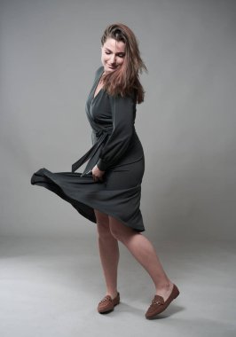 Gri arka planda kendine güvenen, iri yarı genç bir kadının stüdyo portresi.