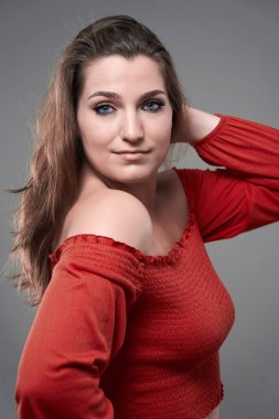 Gri arka planda kendine güvenen, iri yarı genç bir kadının stüdyo portresi.