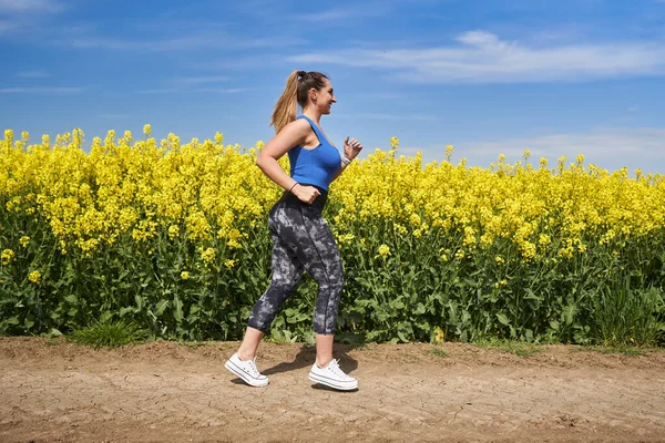 Plus size beautiful latin woman jogging on a dirt road by a canola field