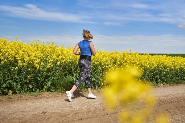 Plus size beautiful latin woman jogging on a dirt road by a canola field