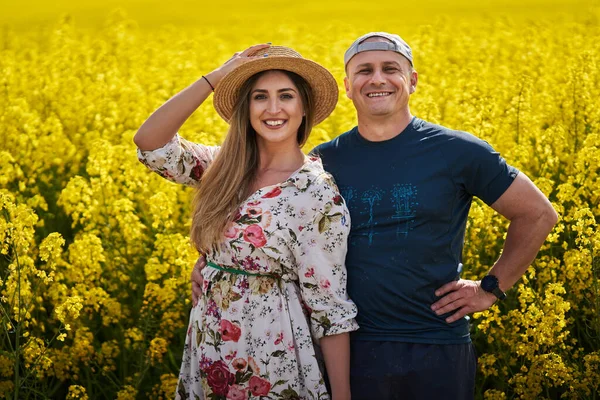 Happy farmers couple standing together by a blossoming canola field