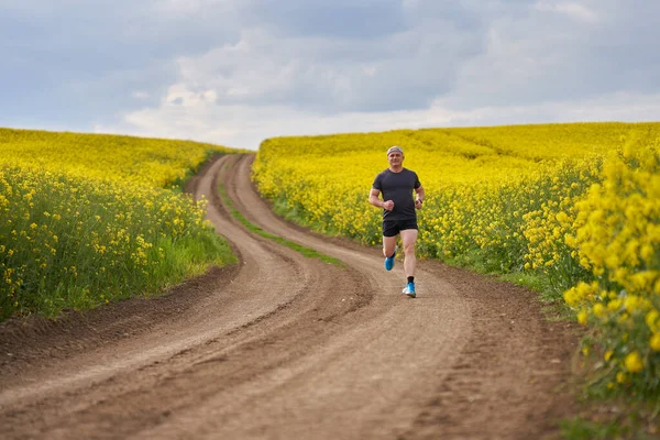 Langstreckenläufer Mittleren Alters Läuft Auf Einem Feldweg Einem Blühenden Rapsfeld — Stockfoto