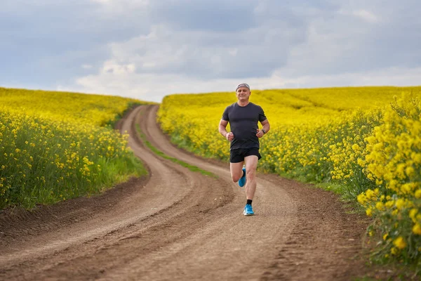 Middle aged distance runner running on a dirt road in a blooming canola field
